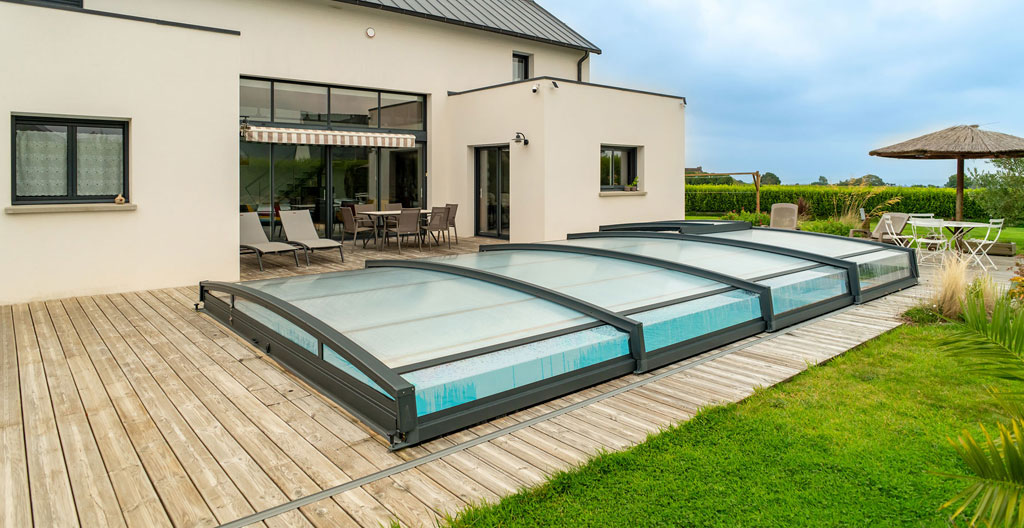 Piscine résidentielle équipée d'un abri télescopique mi-haut en position partiellement ouverte, montrant la structure aluminium et panneaux polycarbonate dans un environnement contemporain